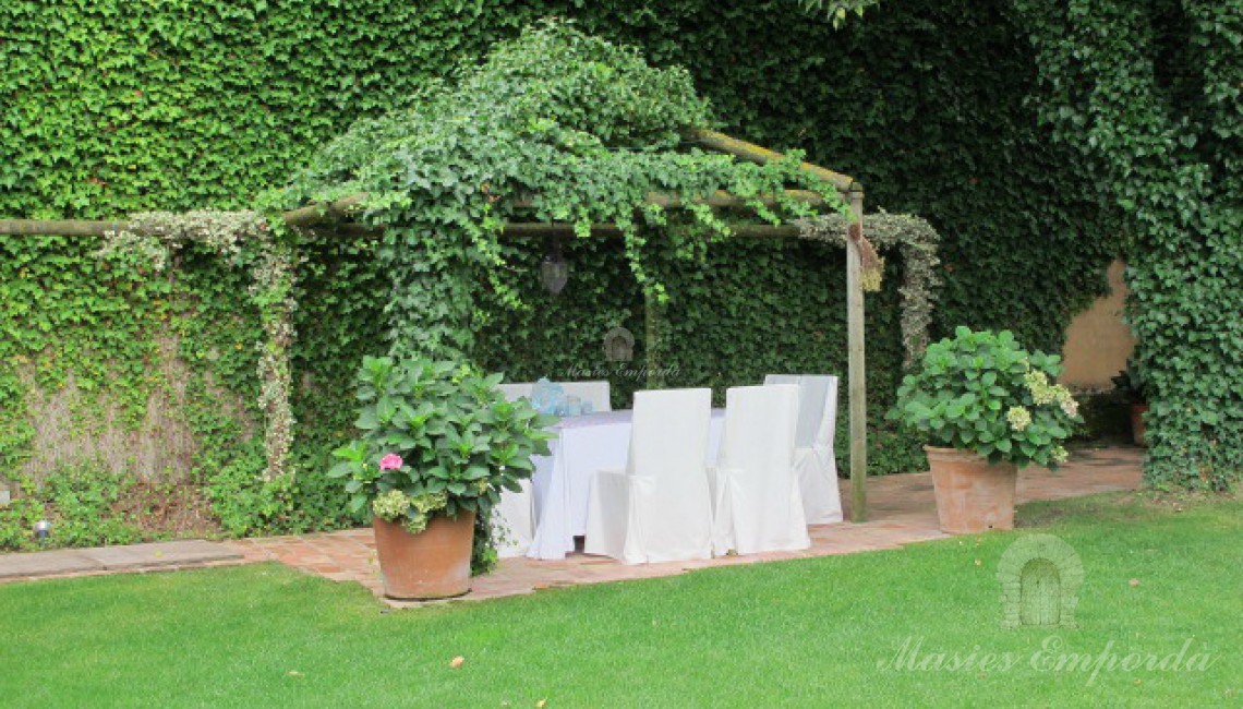 Glorieta del jardín cubierta por yedra trepadora de un verde intenso que contrasta con el suave verde del césped 