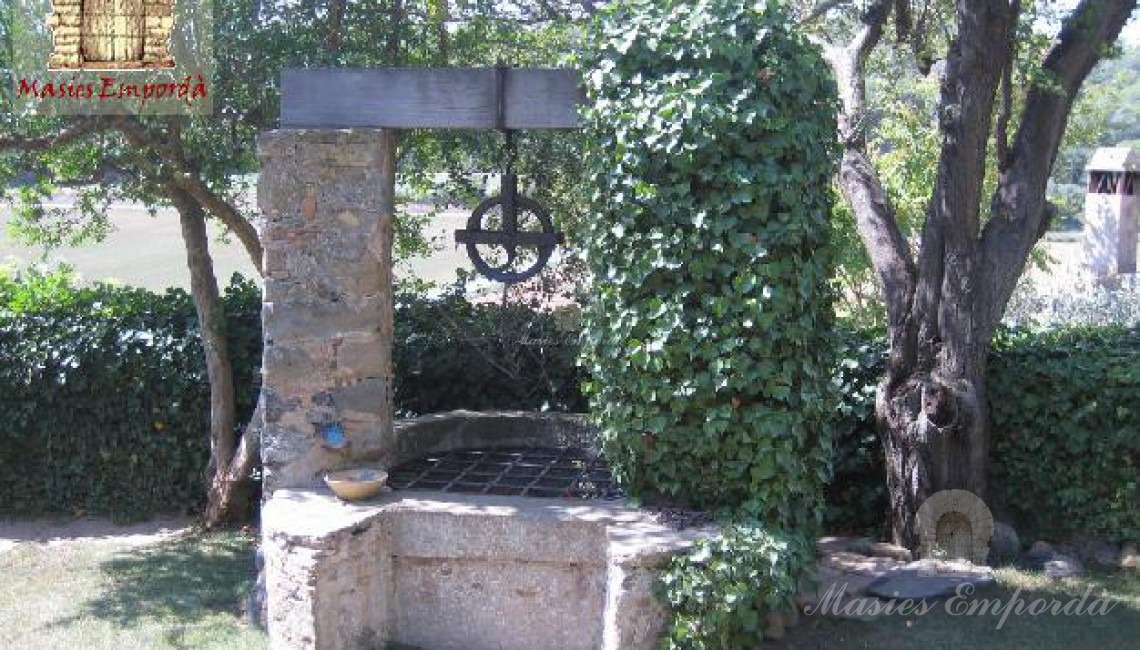 Pozo en el jardín de la propiedad con rueda de forja del mecanismo de recogida de agua de su interior