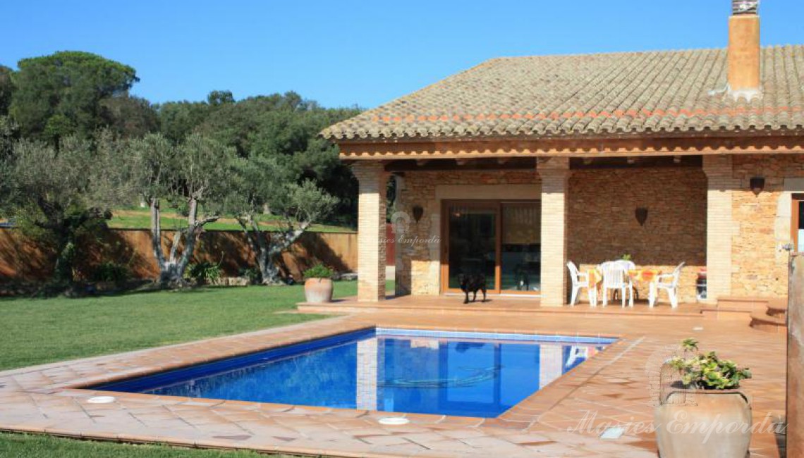 Vista general de la casa con parte del jardín y la piscina en primer plano de la imagen