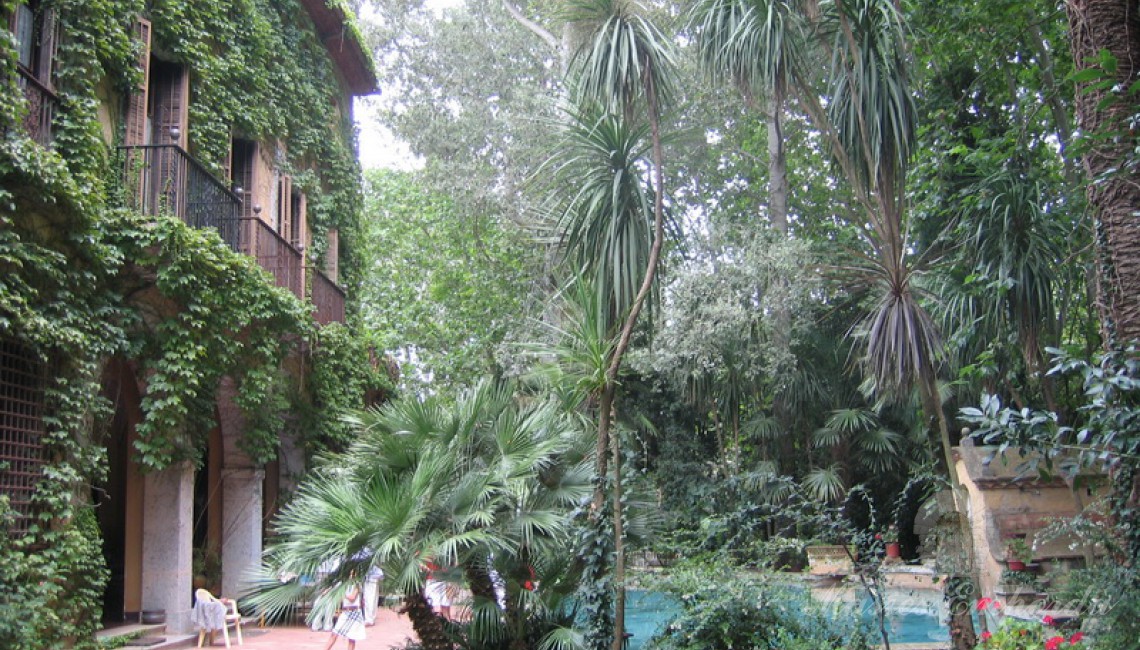 Detalle de la fachada principal de la casa completamente cubierta de yedra trepadora con la piscina en un lateral de la imagen 