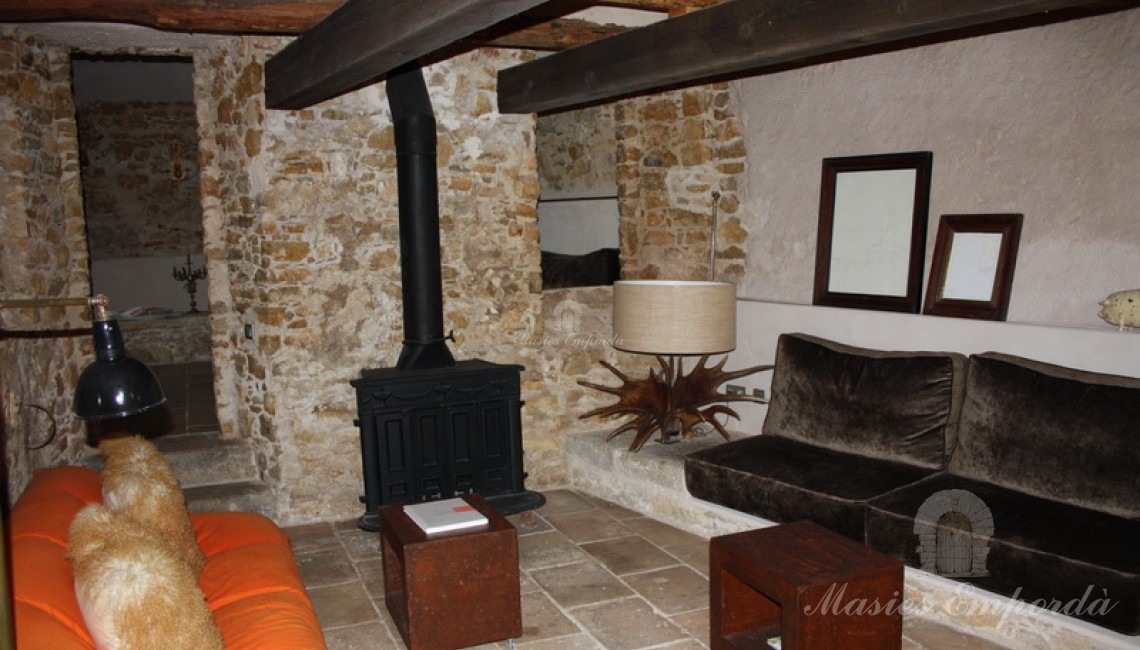 Unos de los salones de planta de la masía con chimenea y cubierta de vigas de madera
