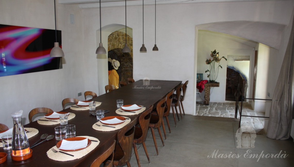 Vista desde el ángulo opuesto al pabellón del  comedor principal de la casa con mesa de hierro corten y el hall de entrada al fondo de la imagen   