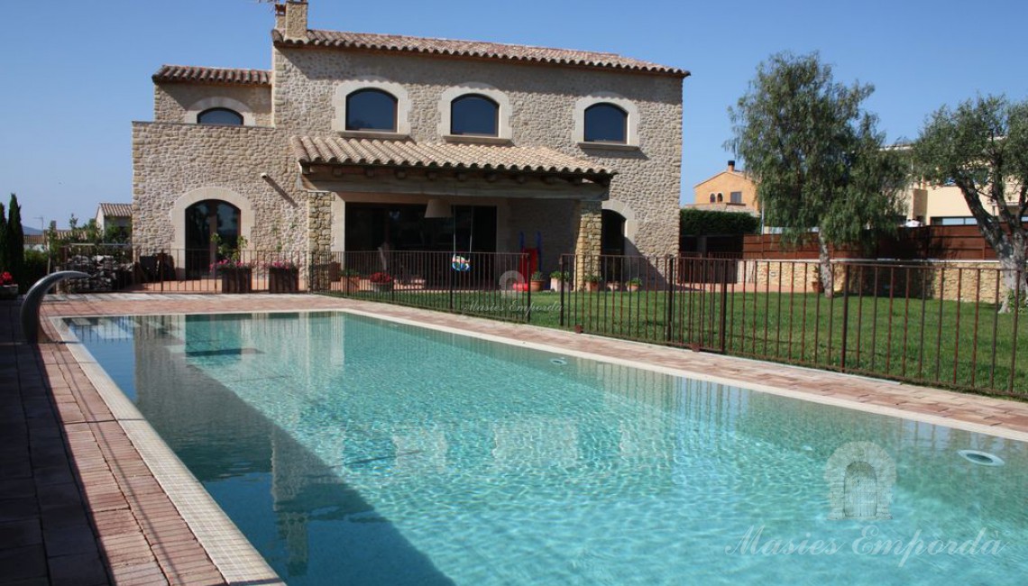 Piscina y jardín de la casa con porche y lateral de fachada al fondo de la imagen