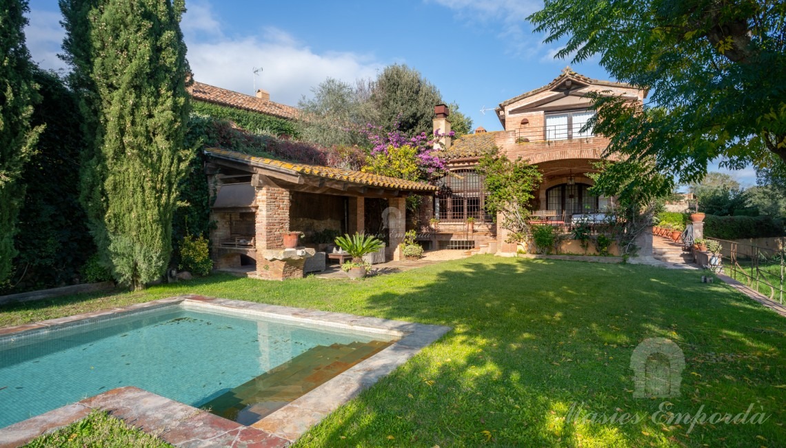 Jardín y el porche de la piscina con barbacoa y la casa al fondo de la imagen