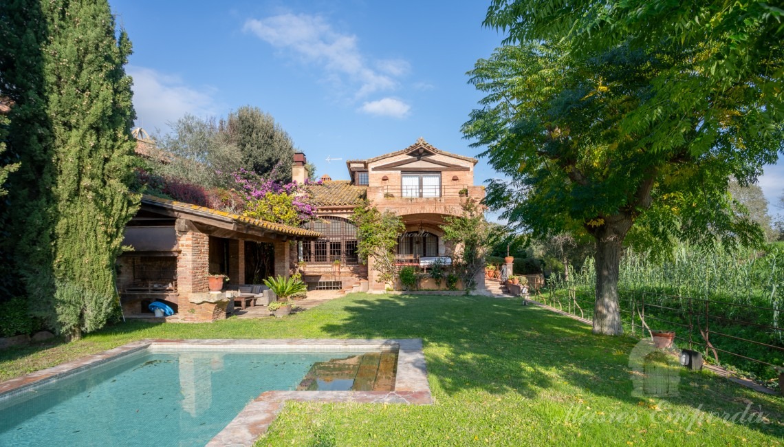 Jardín y el porche de la piscina con barbacoa y la casa al fondo de la imagen