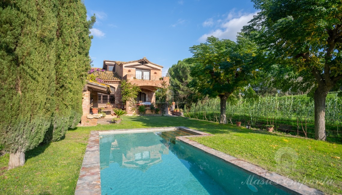 Jardín y el porche de la piscina con barbacoa y la casa al fondo de la imagen