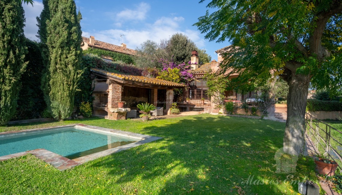 Jardín y el porche de la piscina con barbacoa y la casa al fondo de la imagen 
