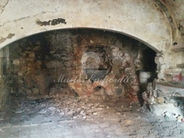 Vista de la cocina con el hogar y el horno bajo cubierta de la chimenea a la izquierda de la imagen y dos vasijas de cenizas para blanquear la ropa