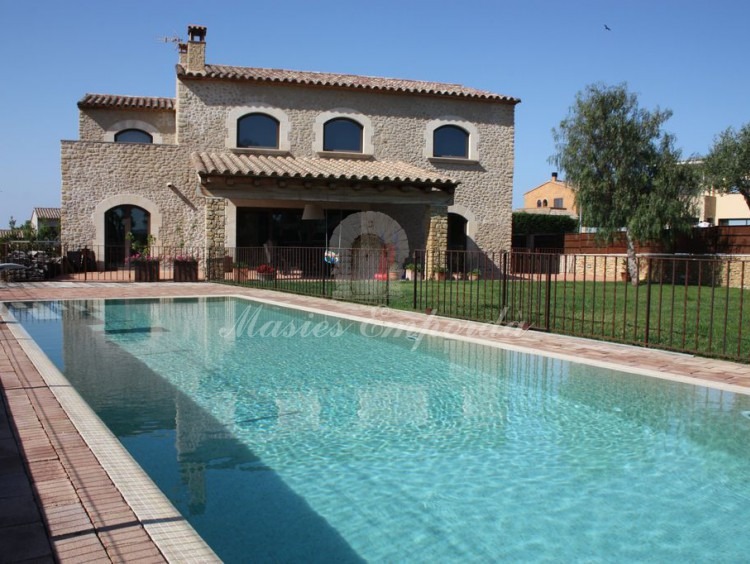 Piscina y jardín de la casa con porche y lateral de fachada al fondo de la imagen