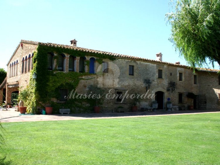 Vista lateral de la masía y los porches anexo a ella rodeada del gran jardín y al fondo la antigua torre de defensa la propiedad que está ubicada Regencos Baix Empordà