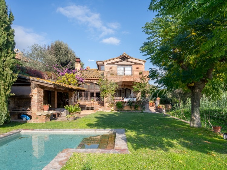 Jardín y el porche de la piscina con barbacoa y la casa al fondo de la imagen