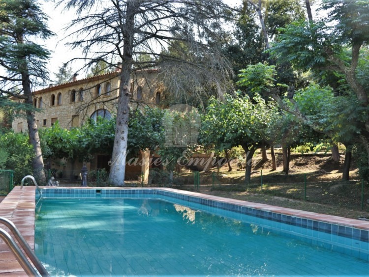Vista de la piscina, jardín y la masía al fondo de la imagen